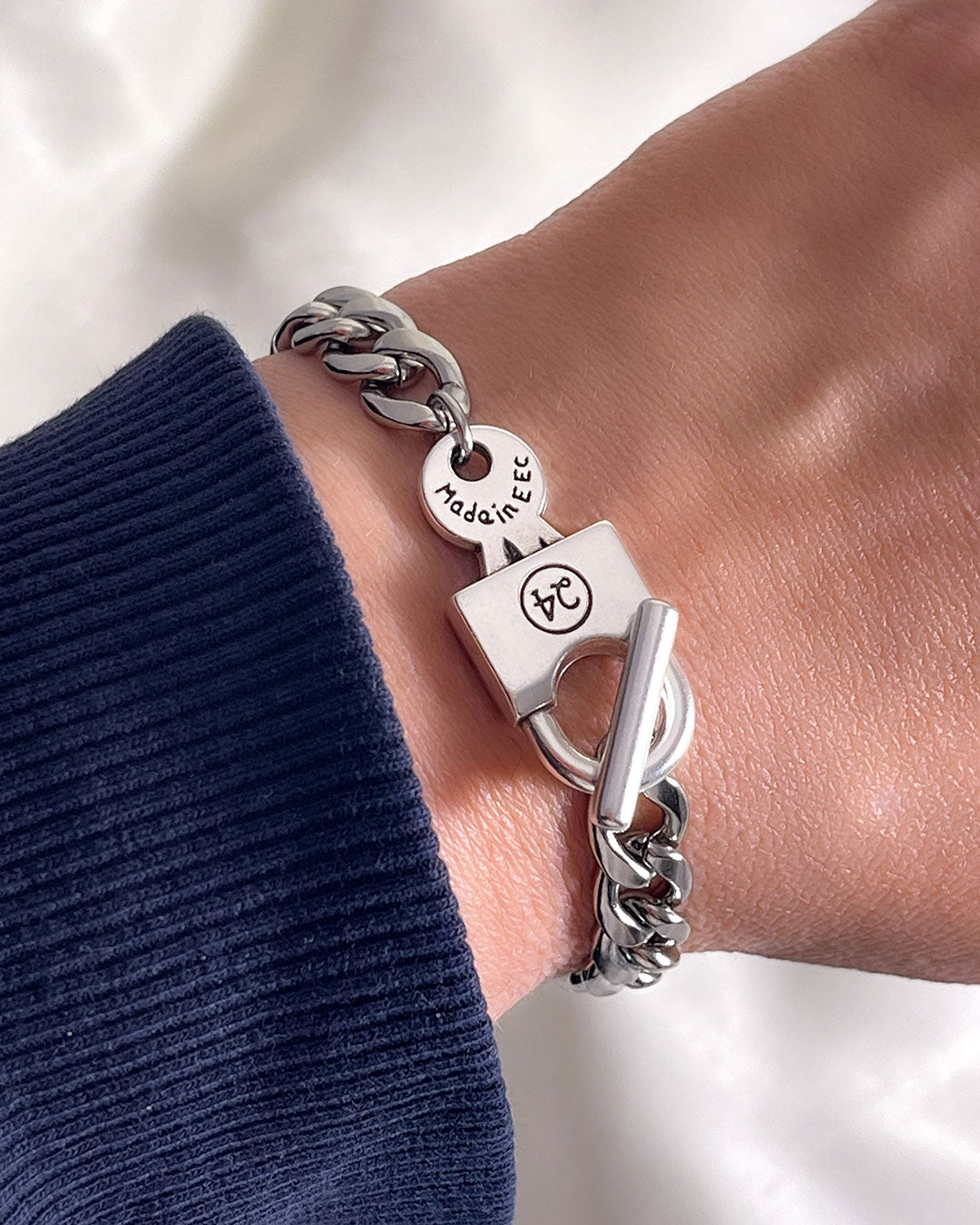 Silver chain bracelet with a padlock clasp on the wrist against a neutral background