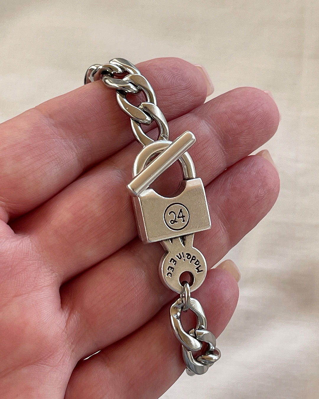 Silver chain bracelet with a padlock clasp held in a hand against a neutral background
