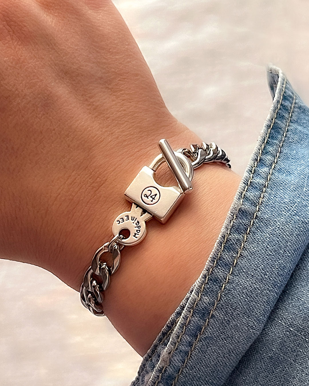 Silver chain bracelet with padlock clasp on a wrist against a blurred background