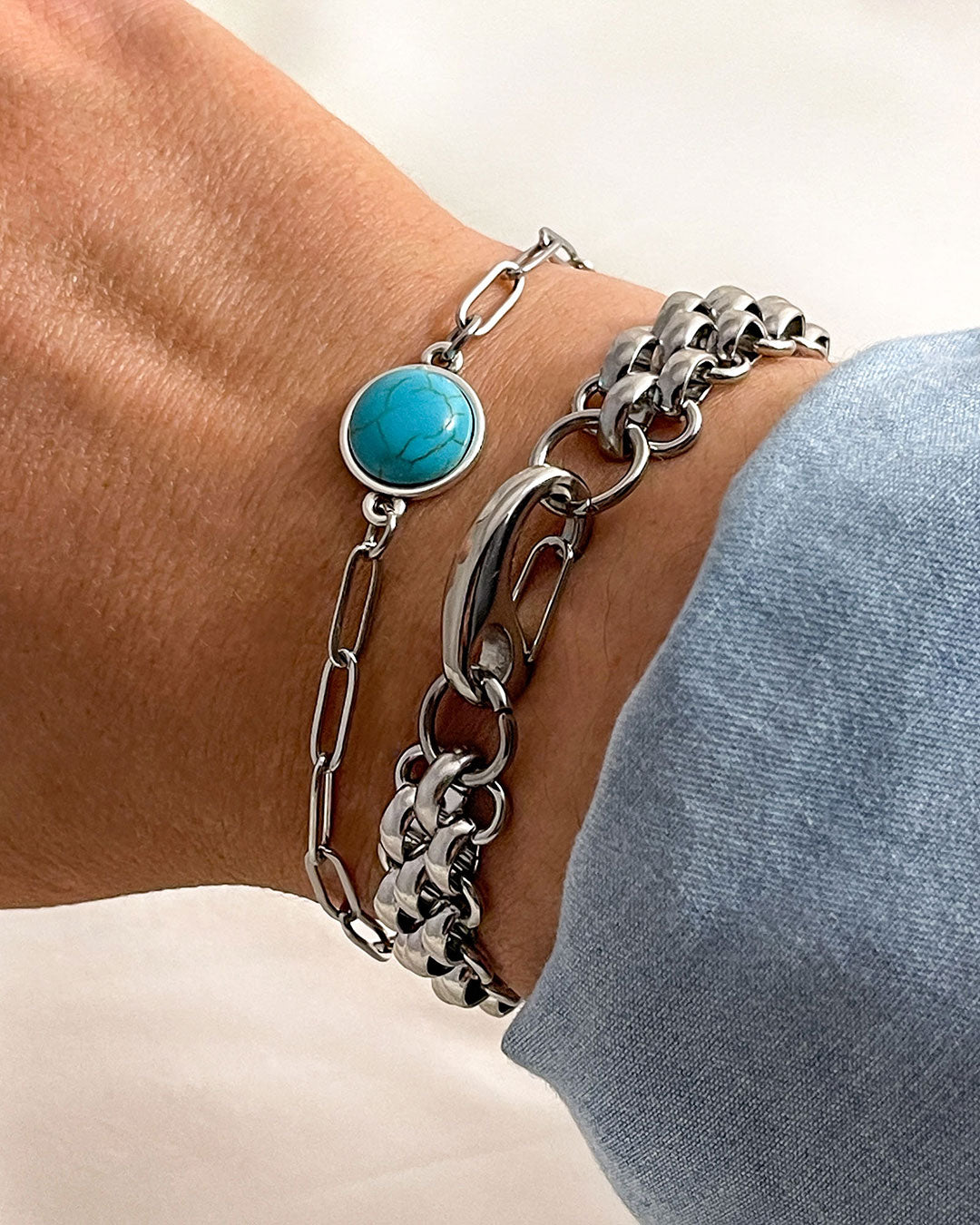 Silver chain bracelets, one with a turquoise stone on a wrist against a light background