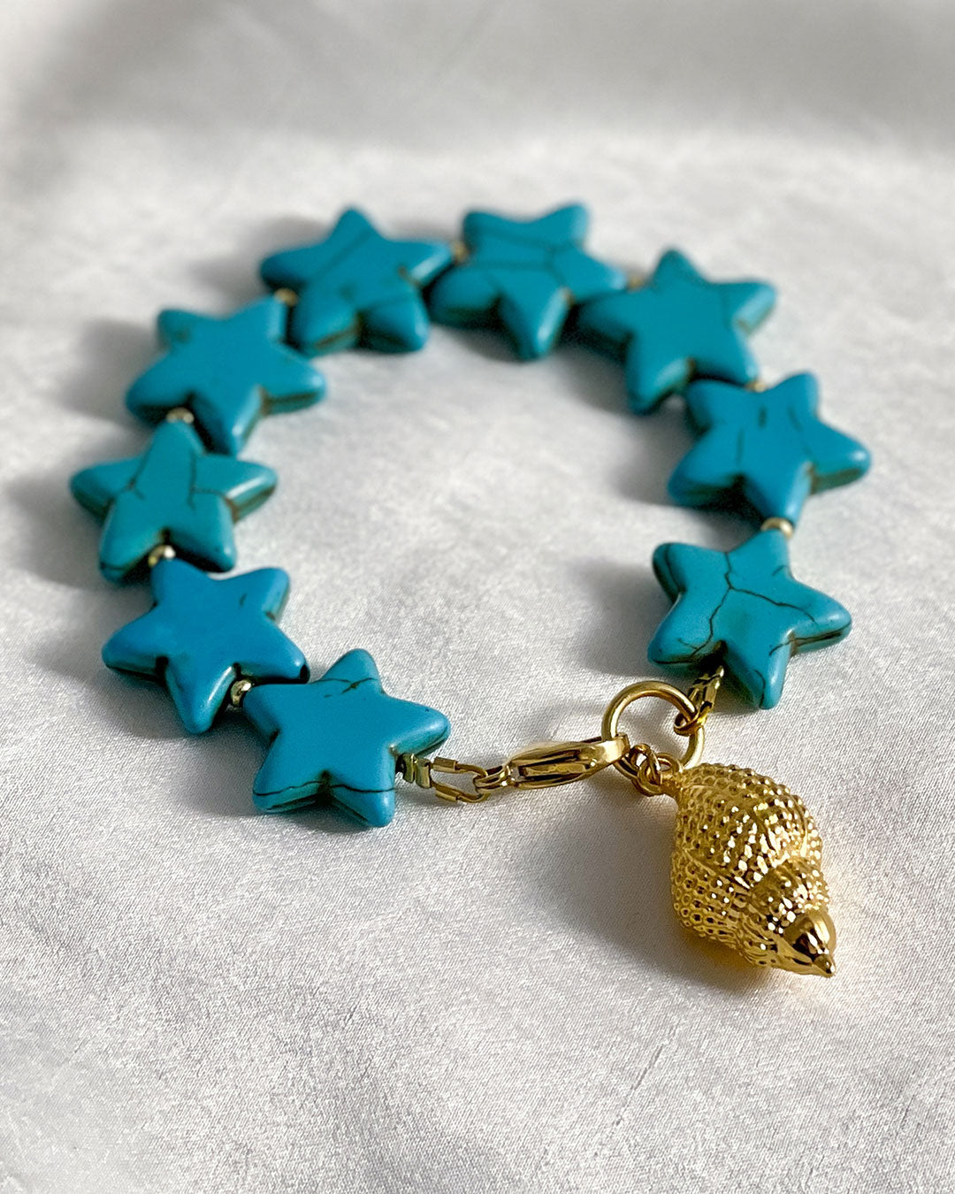 Turquoise star-shaped bracelet with a gold shell charm on a natural background