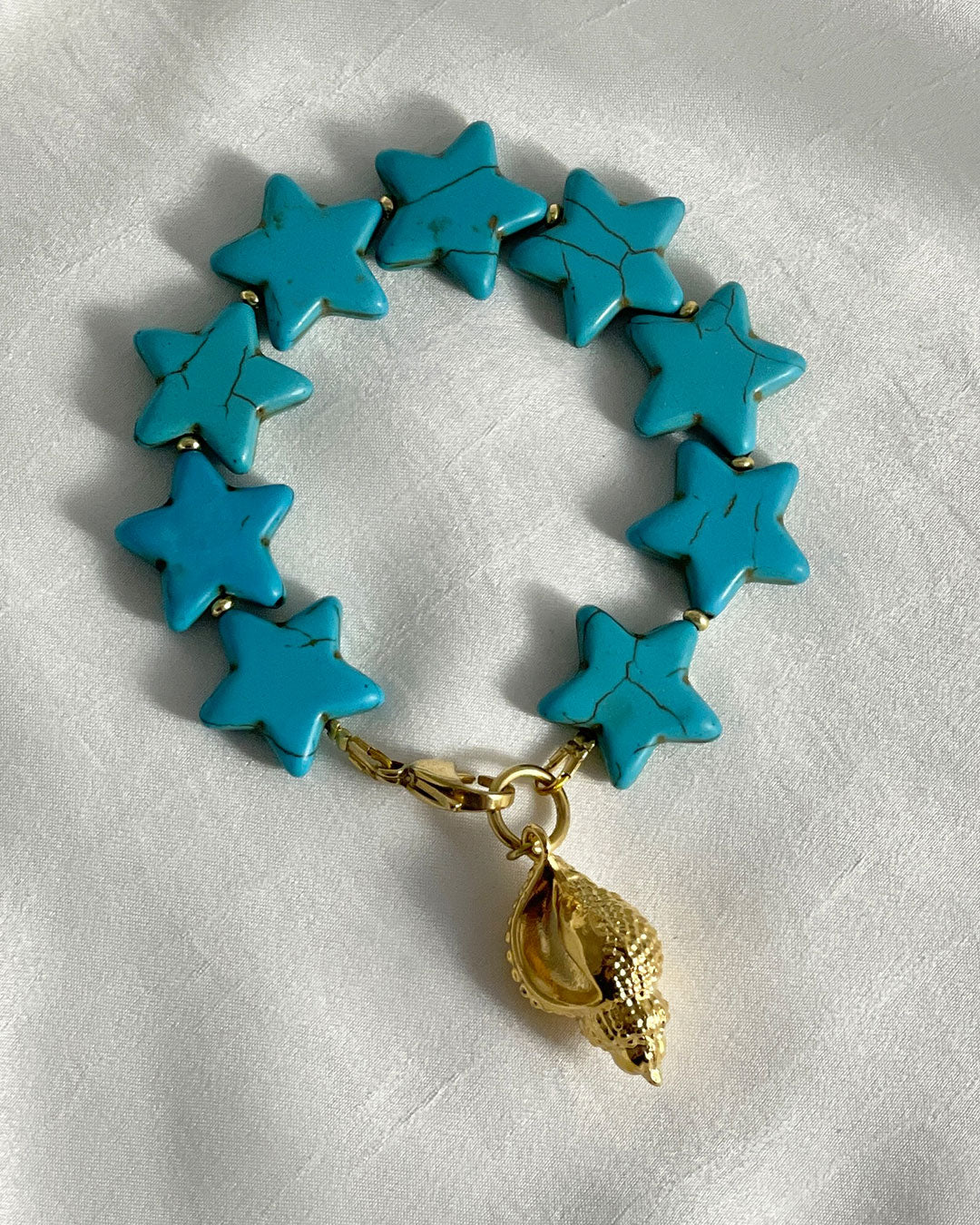 Turquoise star-shaped bracelet with a gold shell charm on a white fabric background
