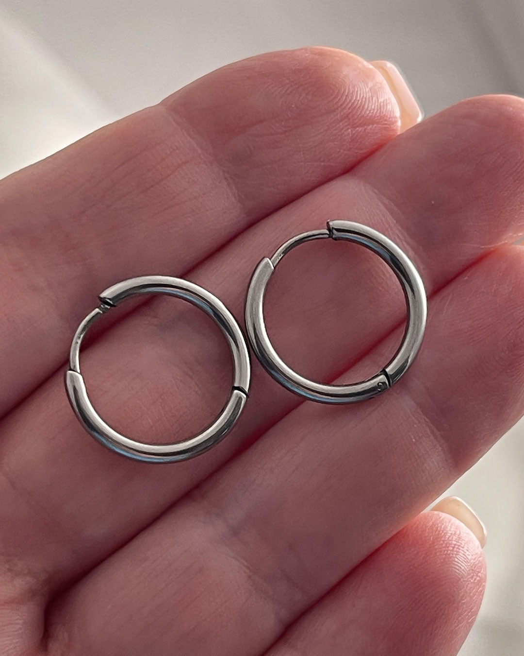 Pair of silver hoop earrings 14mm held between fingers against a neutral background