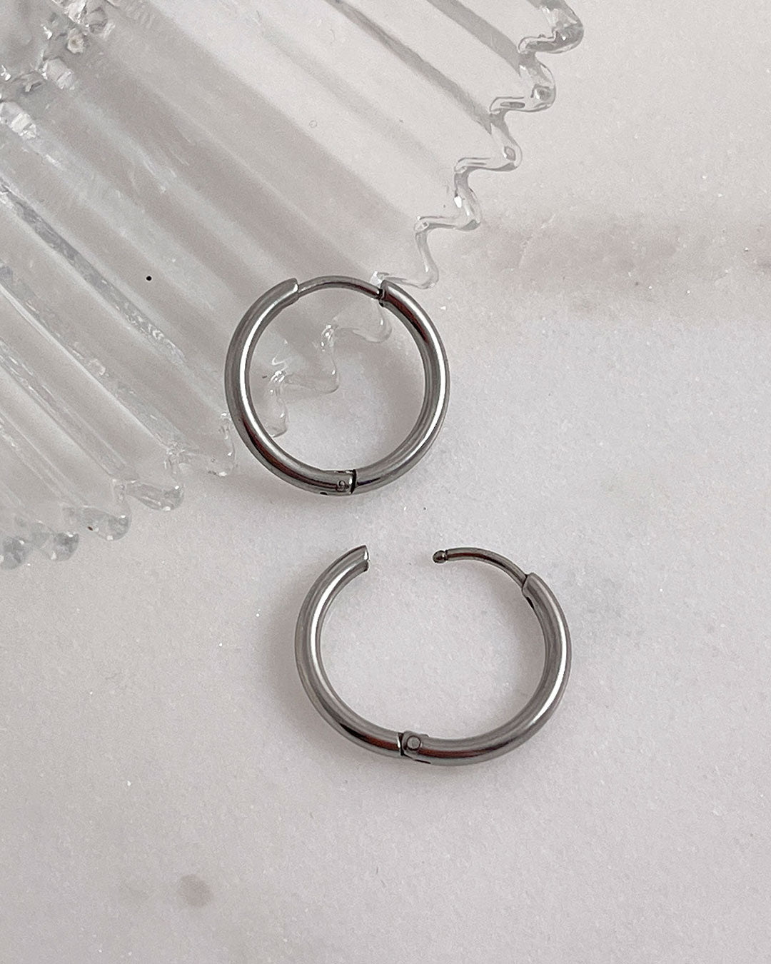 Pair of silver hoop earrings 14mm on a light gray surface.