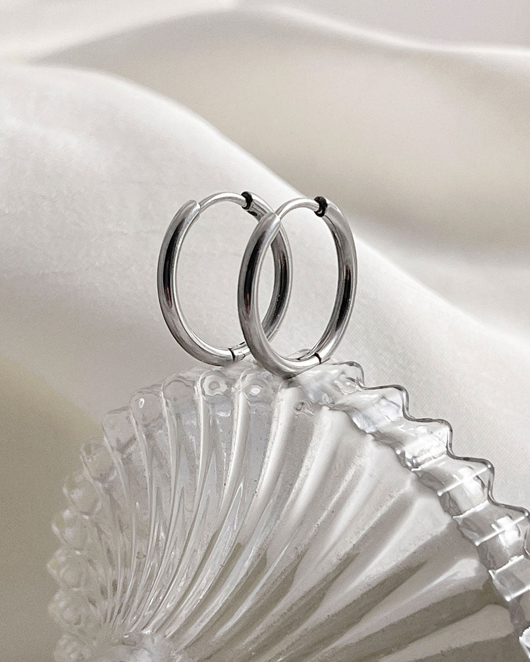 Silver hoop earrings 14mm on a white fabric background