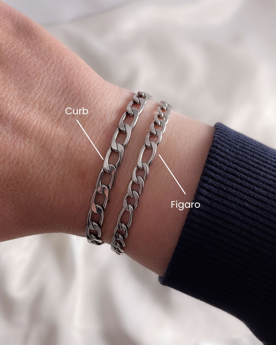 Model wearing two silver chain bracelets with different link styles. The bracelets are all different widths and have a curb chain and a figaro chain design.