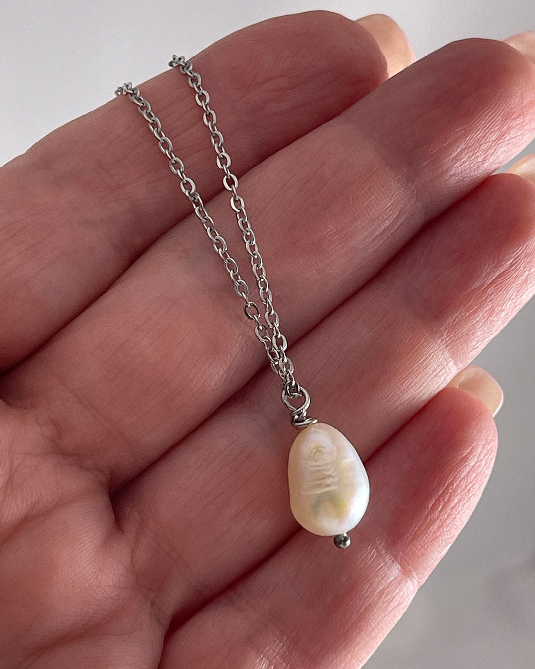Silver necklace with a single pearl pendant held in a hand against a neutral background