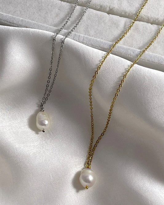 Two pearl necklaces, one silver and one gold, on a white fabric background