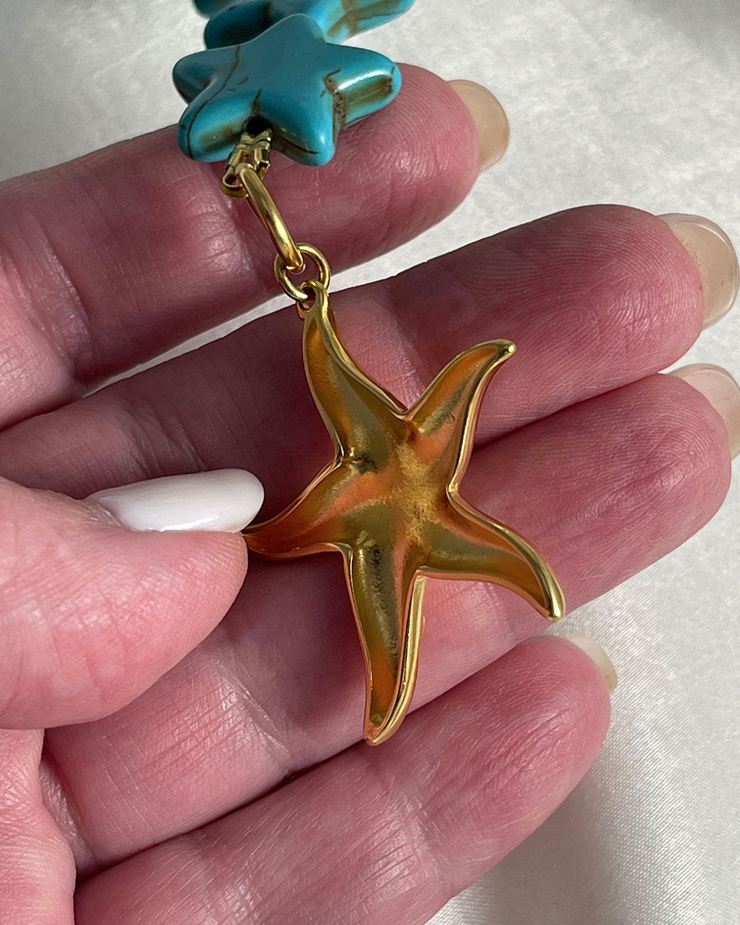 Close up details from the back of a turquoise star-shaped howlite beaded bracelet with a gold starfish charm