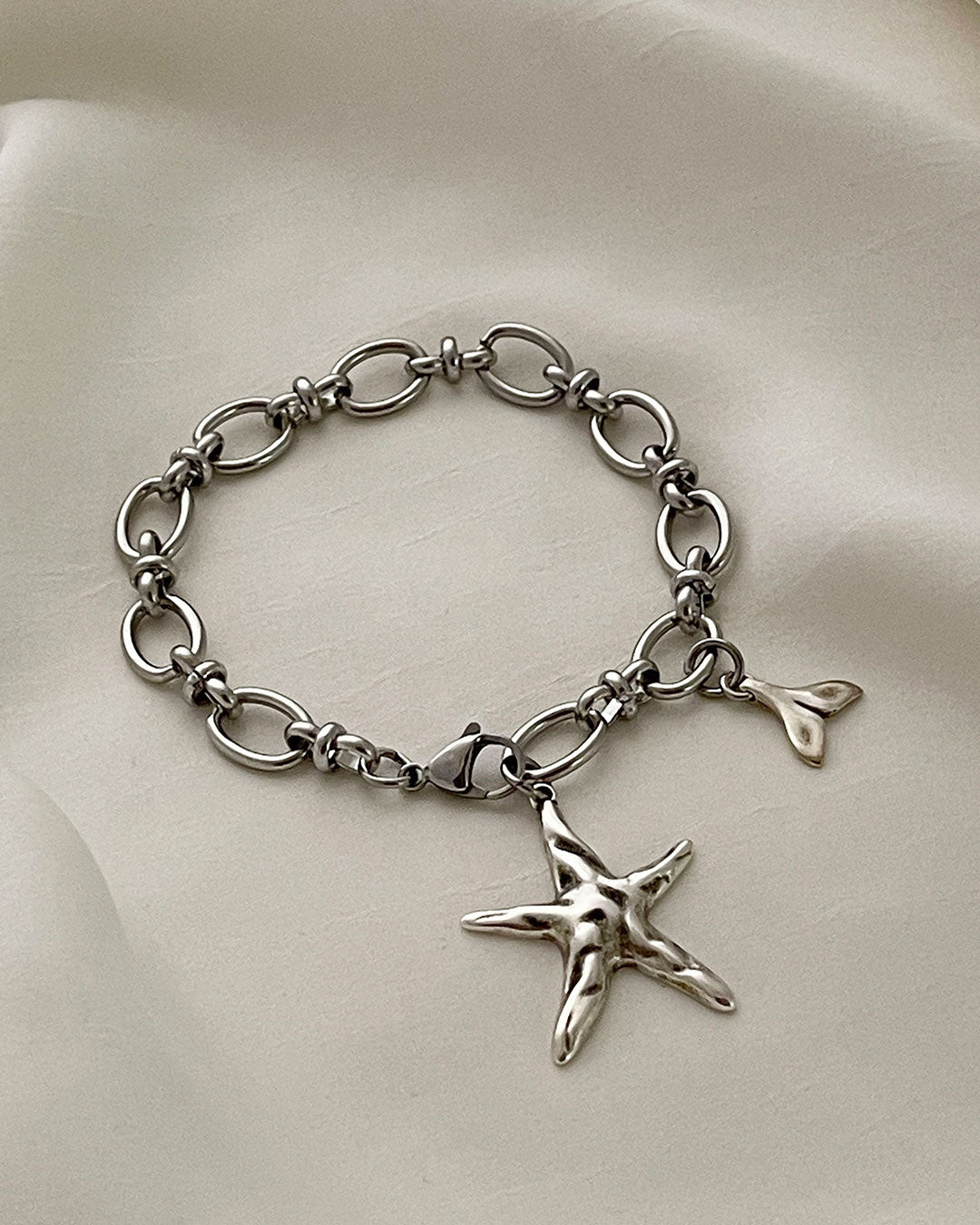 Silver bracelet with a starfish charm on a beige fabric background
