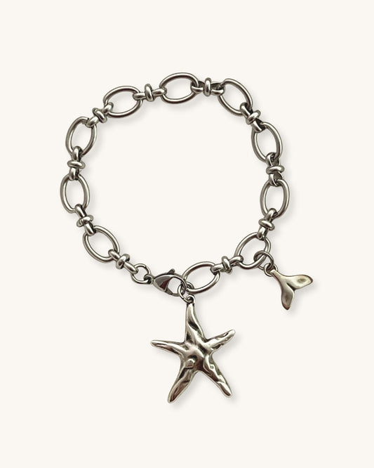 Silver bracelet with a starfish charm on a beige fabric background