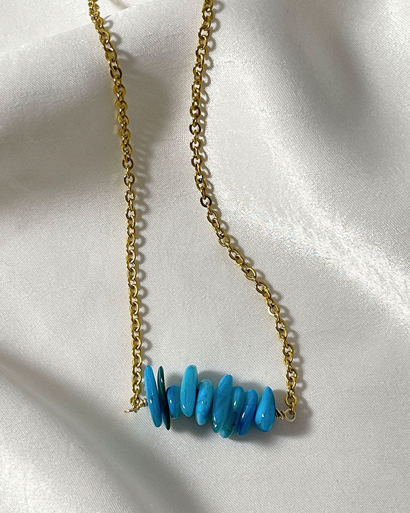 A gold dainty chain necklace with a cluster of turquoise chip stones in the middle.