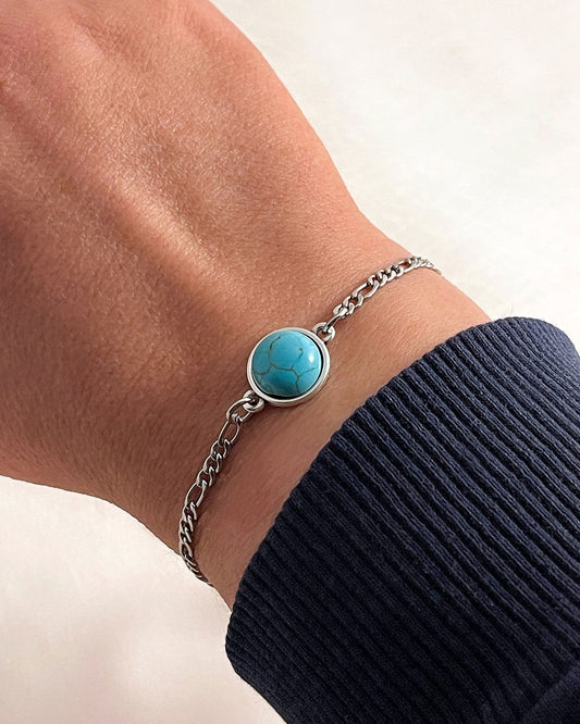 Turquoise stone bracelet with figaro chain in silver on a wrist with a black sleeve against a white background