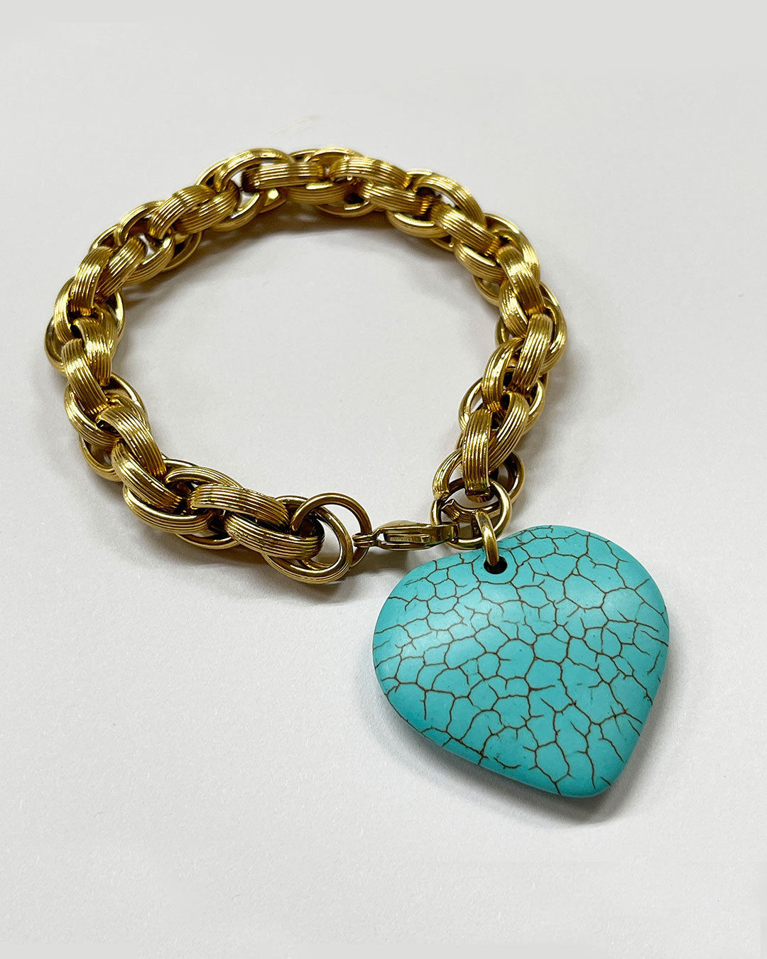 A gold chunky chain bracelet with a large turquoise gemstone heart charm