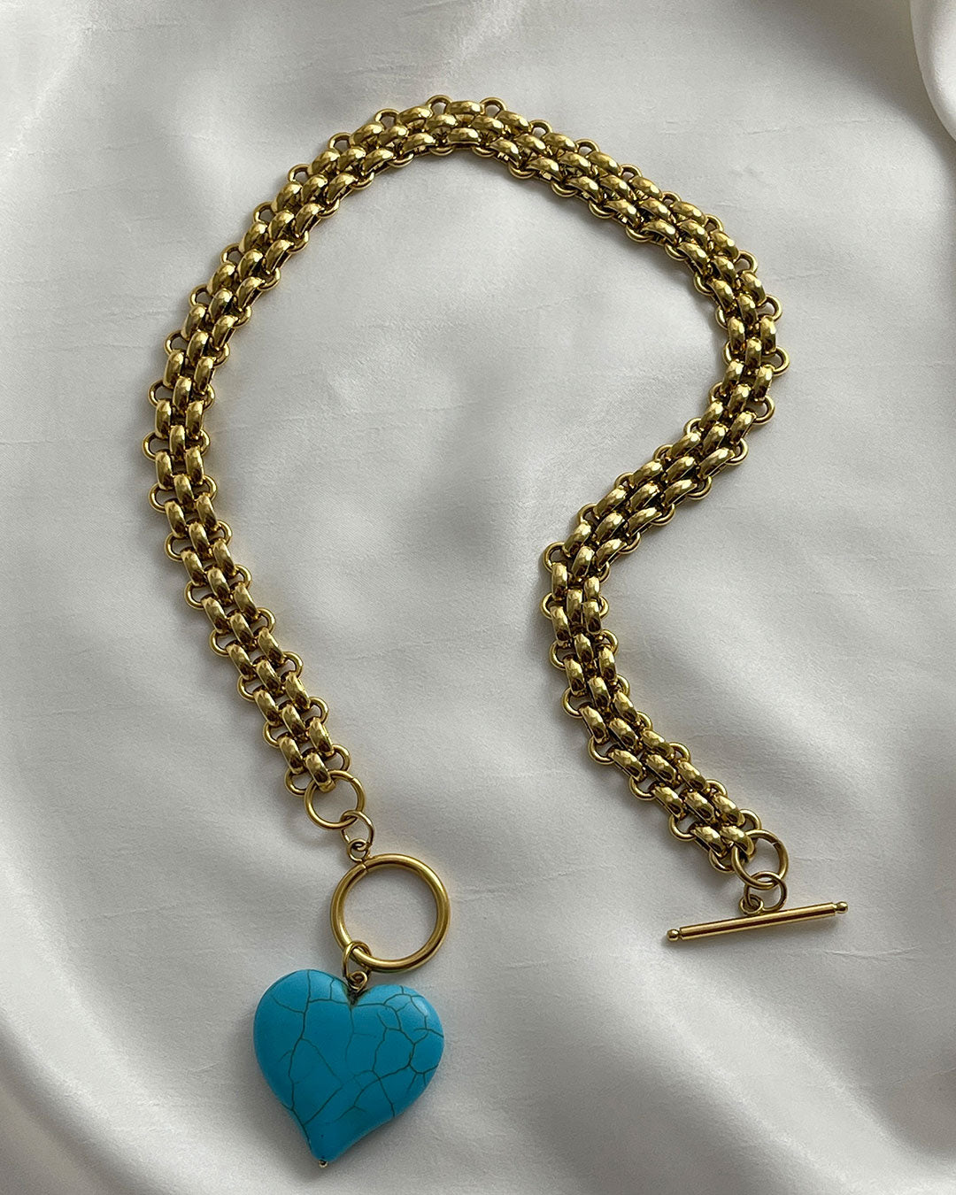 Chunky gold chain necklace with a turquoise heart pendant on a white fabric background
