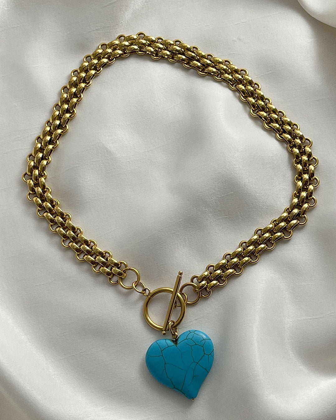 Chunky gold chain necklace with a turquoise heart pendant on a white fabric background