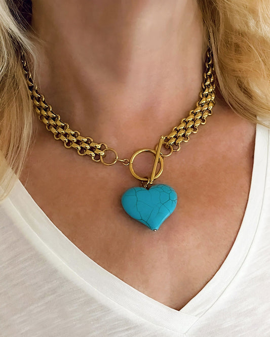 Chunky gold chain necklace with a turquoise heart pendant worn by a person in a white shirt.