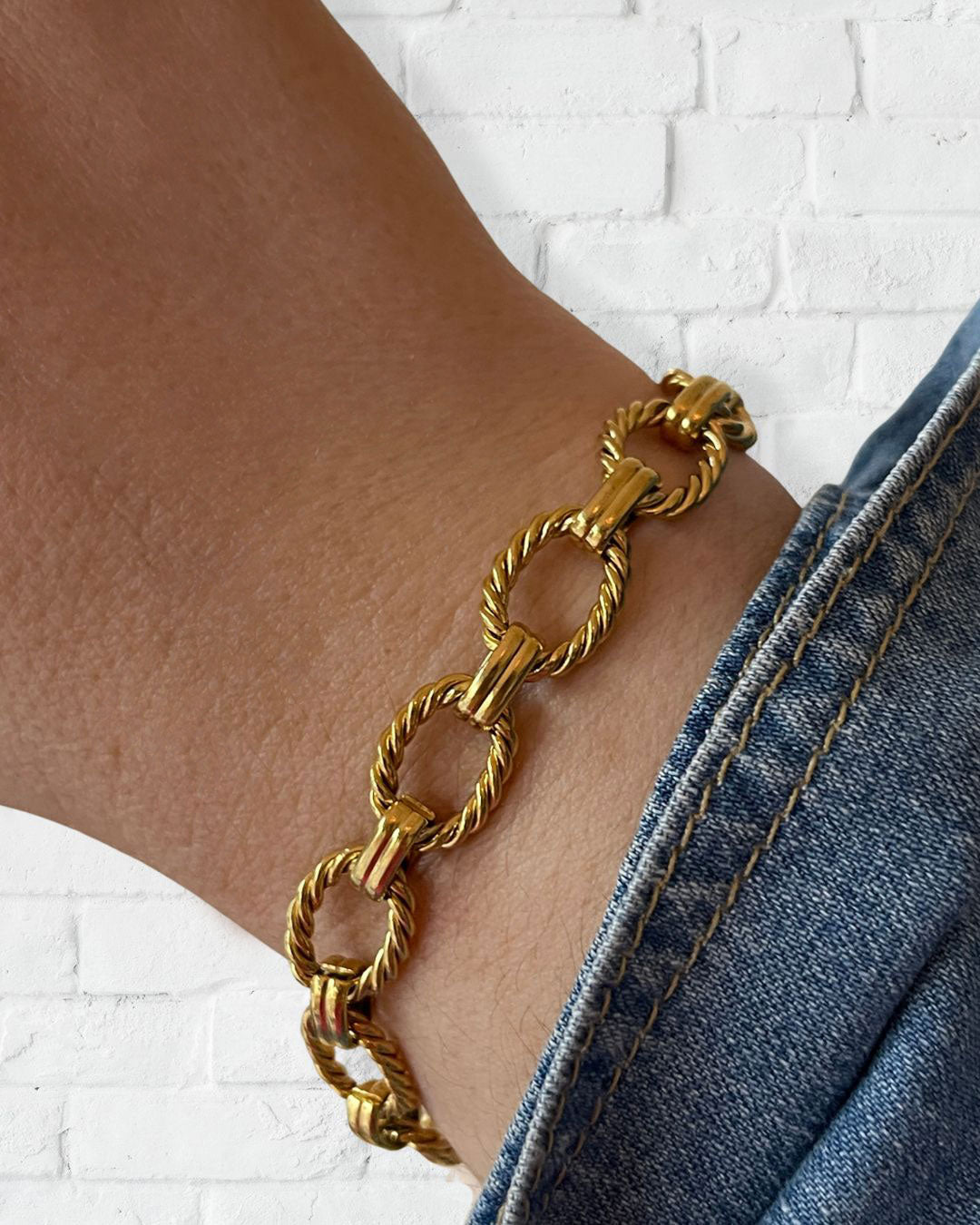 Wrist with a gold chain bracelet with twisted links and a clasp closure