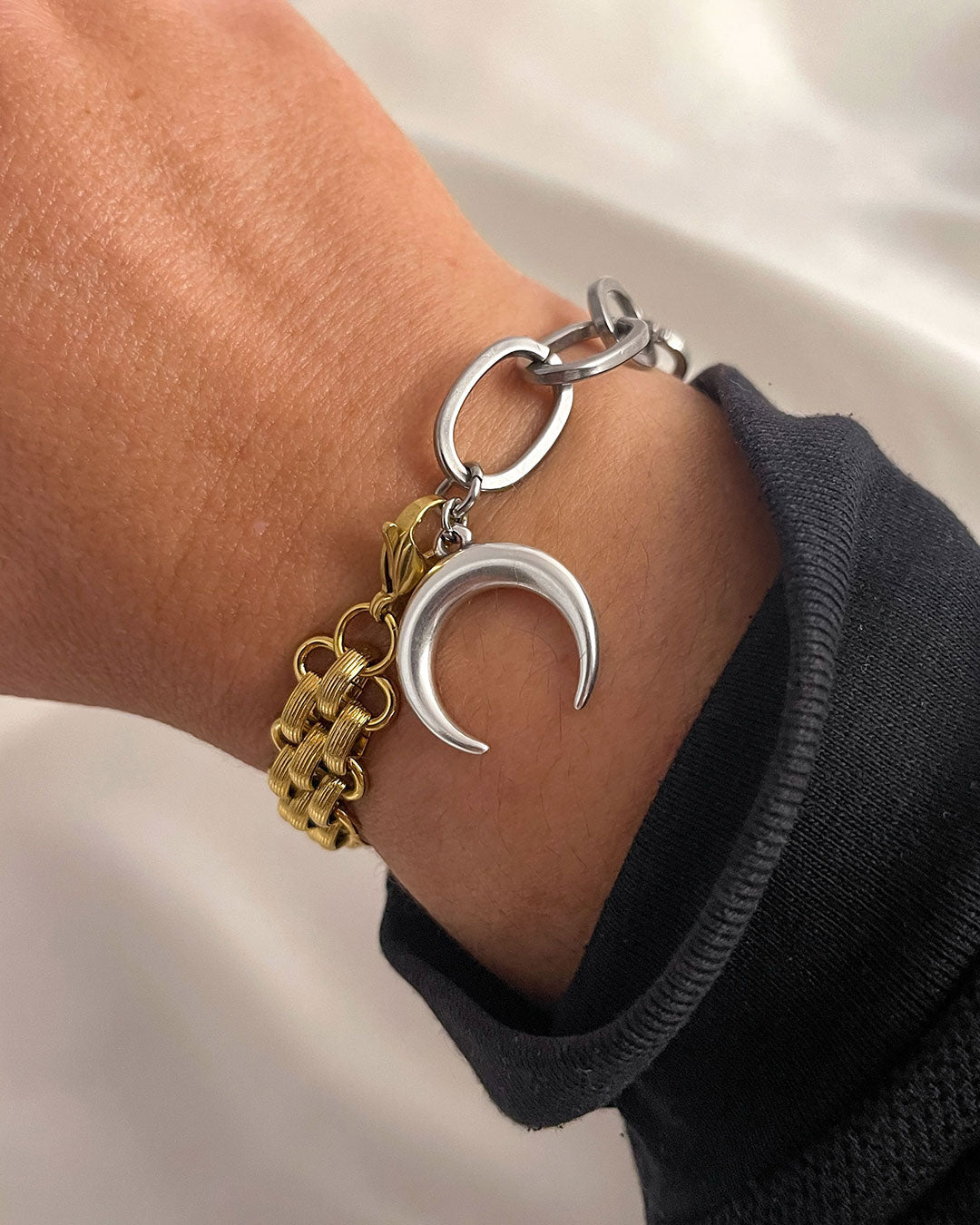 Gold and silver bracelet with a crescent moon charm on a wrist against a neutral background