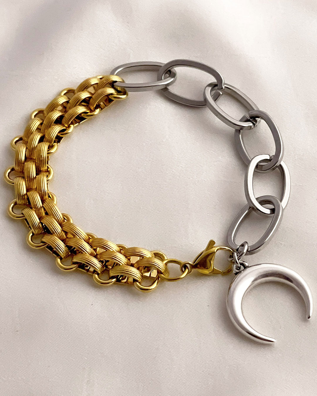 Bracelet with gold and silver chain links and a moon charm on a light background