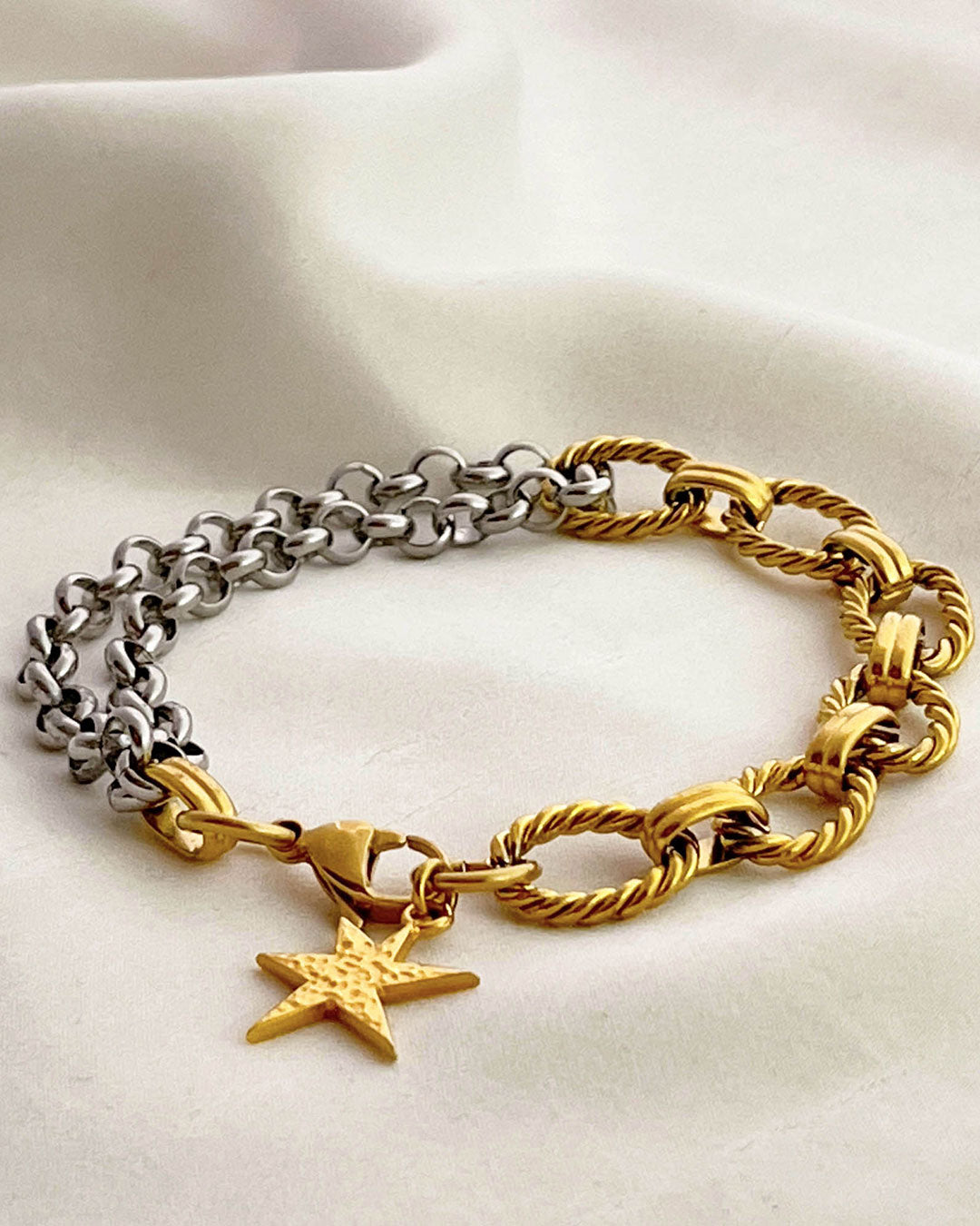 Two chain bracelets, one gold and one silver with a gold charm charm on a light background