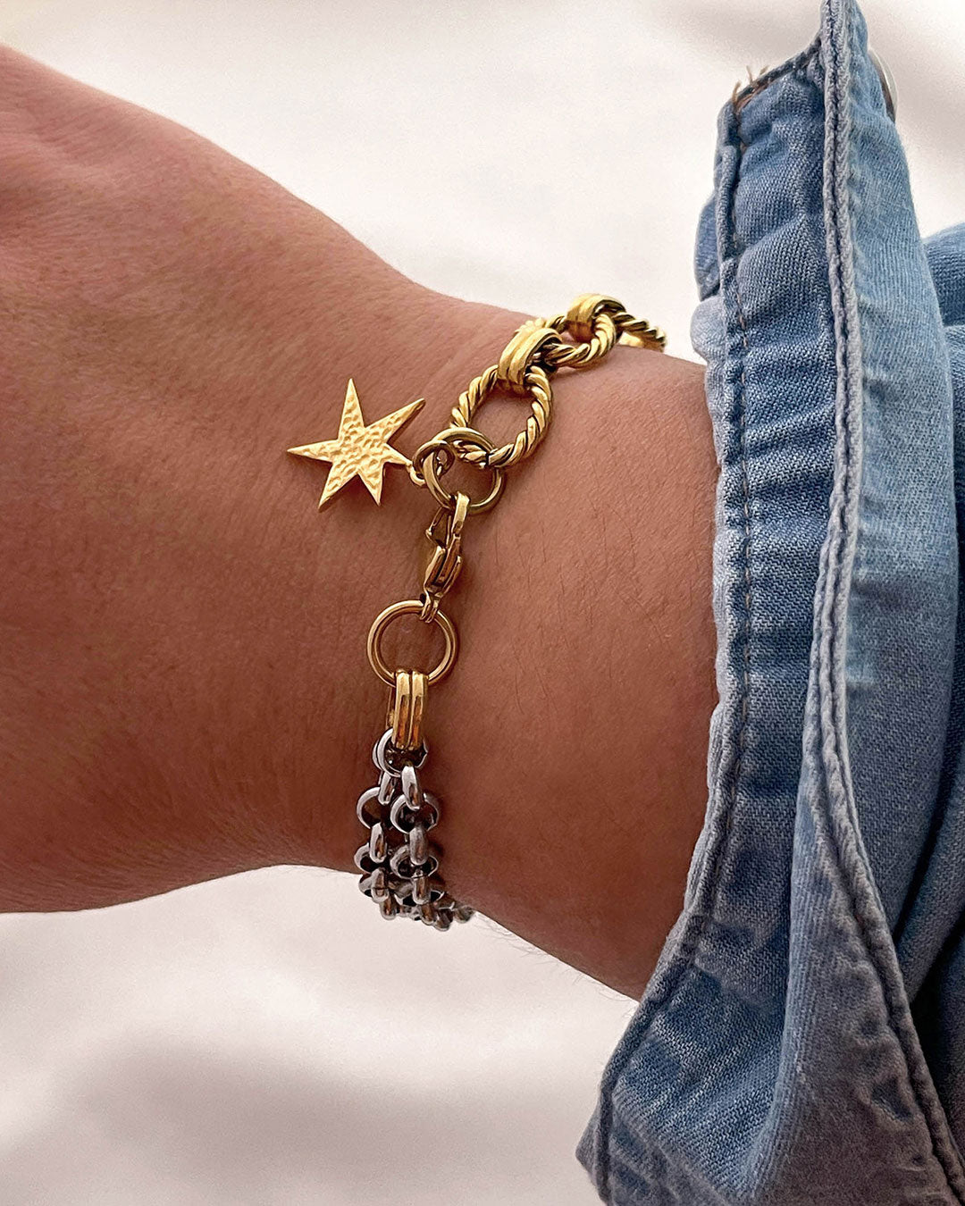 Gold and silver chain bracelet with a star charm on a wrist, against a light background.