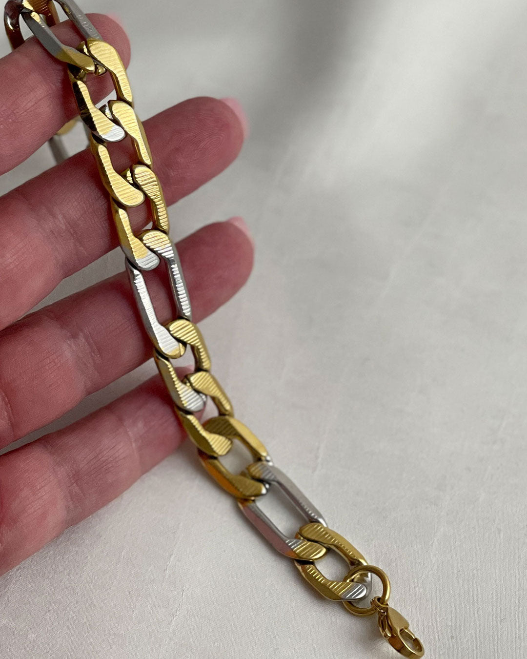 Gold and silver chain bracelet held by a hand on a light background
