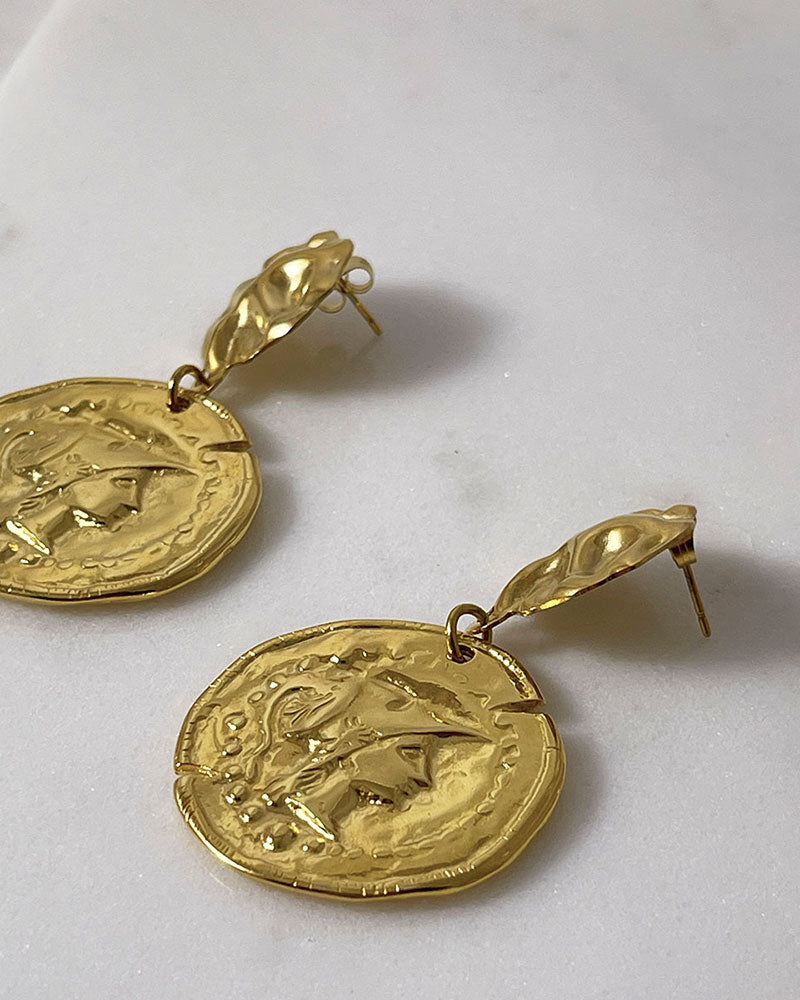 The Athena Coin Earrings, a pair of gold earrings featuring a raised design of Athena's goddess face accents on a coin.