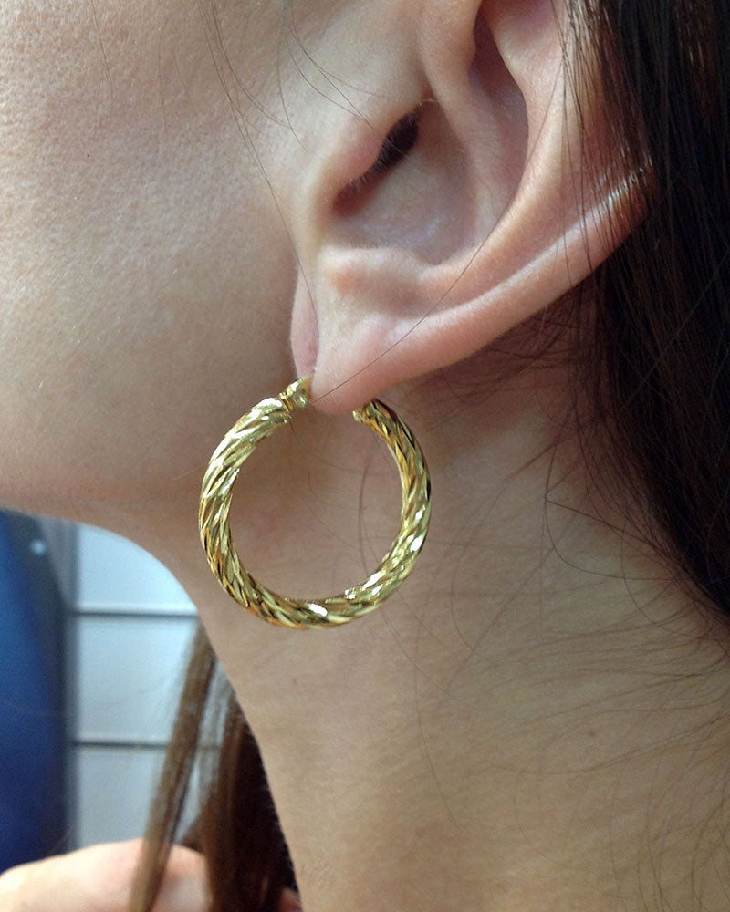 Model wearing a pair of 30mm twisted gold hoop earrings