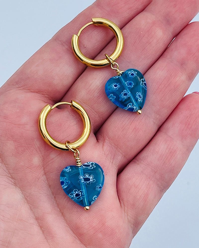 Gold hoop earrings with blue heart pendants on a hand