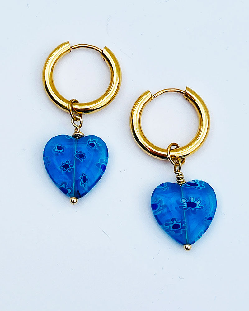 Gold hoop earrings with blue heart pendants on a grey background