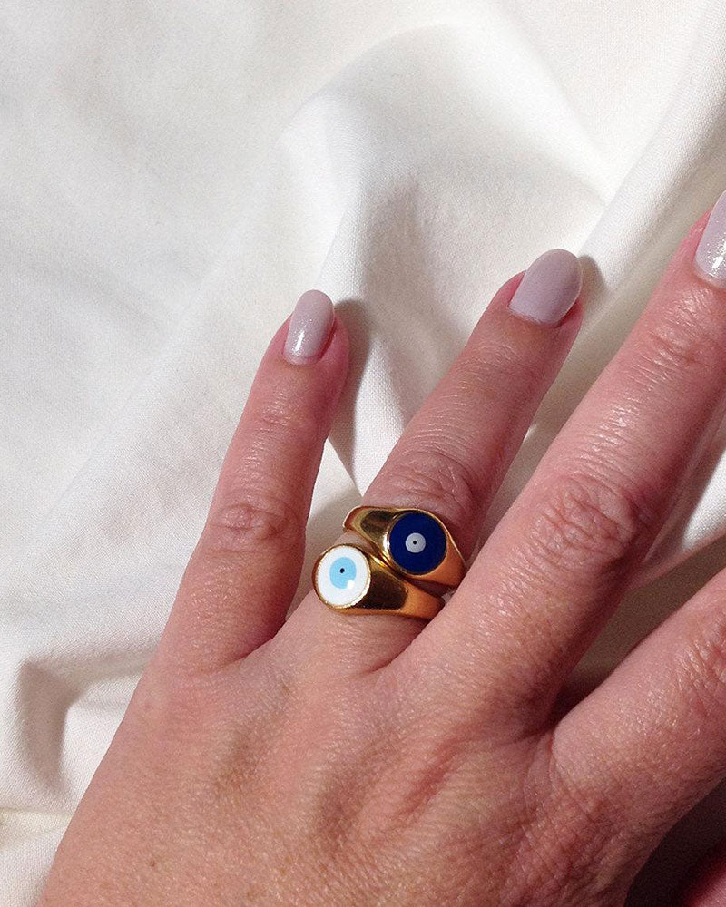 Gold evil eye rings in white and blue on a finger
