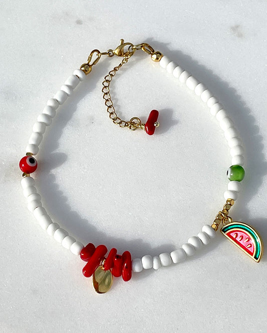 A white glass beaded anklet adorned with a watermelon charm and coral shell beads