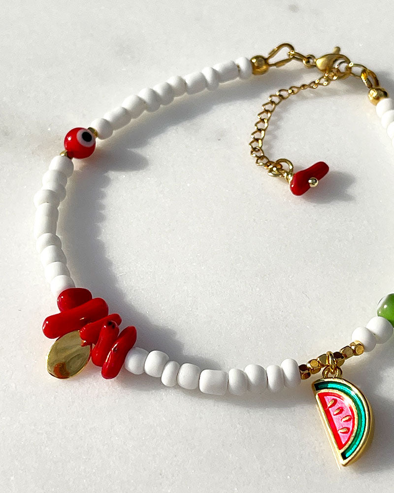 A white glass beaded anklet adorned with a watermelon charm and coral shell beads