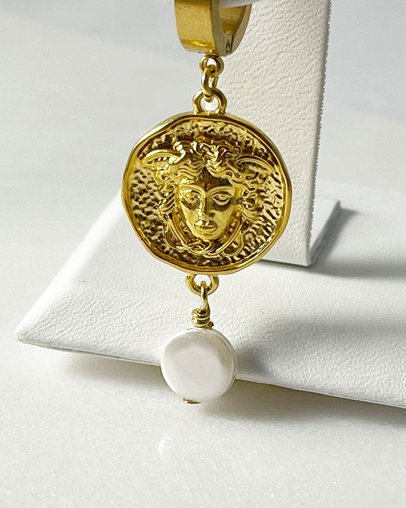 The Medusa Hoop Earrings, a pair of gold hoop earrings adorned with a medusa round charm and a MOP shell pearl.