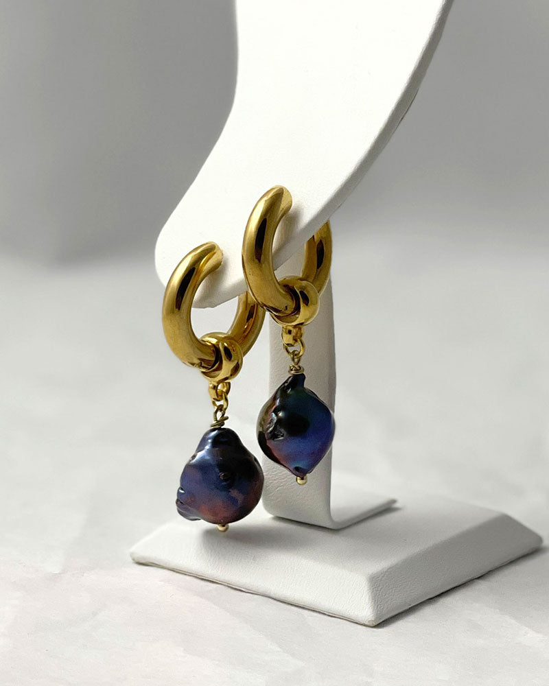 The Black Baroque Pearl Hoops, a pair of gold stainless steel hoop earrings adorned with irregular-shaped black pearls.
