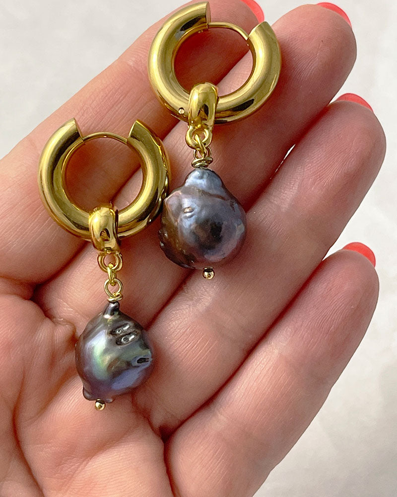 The Black Baroque Pearl Hoops, a pair of gold stainless steel hoop earrings adorned with irregular-shaped black pearls.