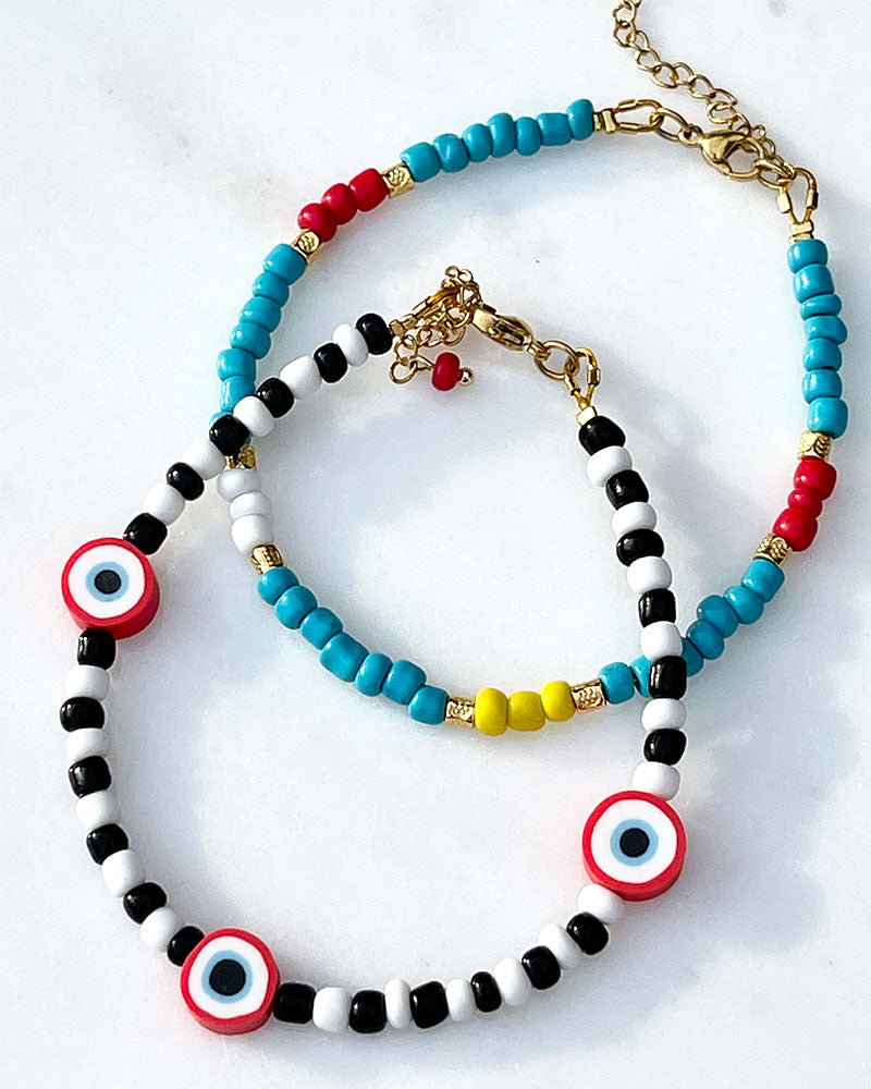 A Rainbow Beaded Summer Anklet adorned with gold metal beads and a black & white beaded anklet with red evil eye beads