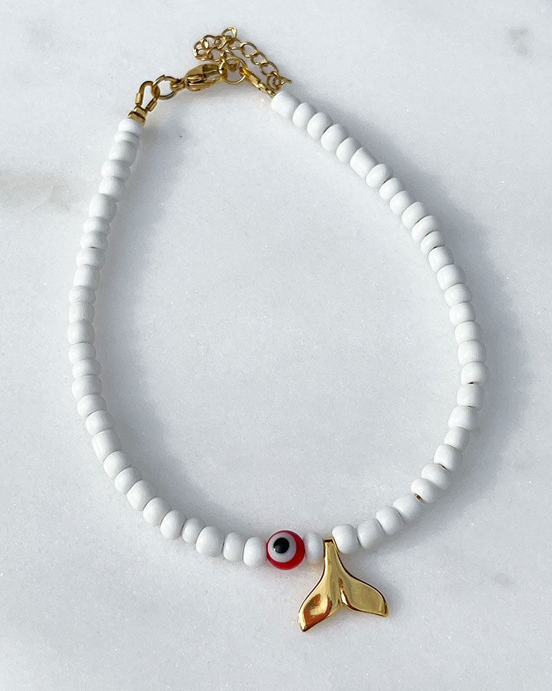 A white glass beaded anklet adorned with a gold tail and a colorful evil eye bead