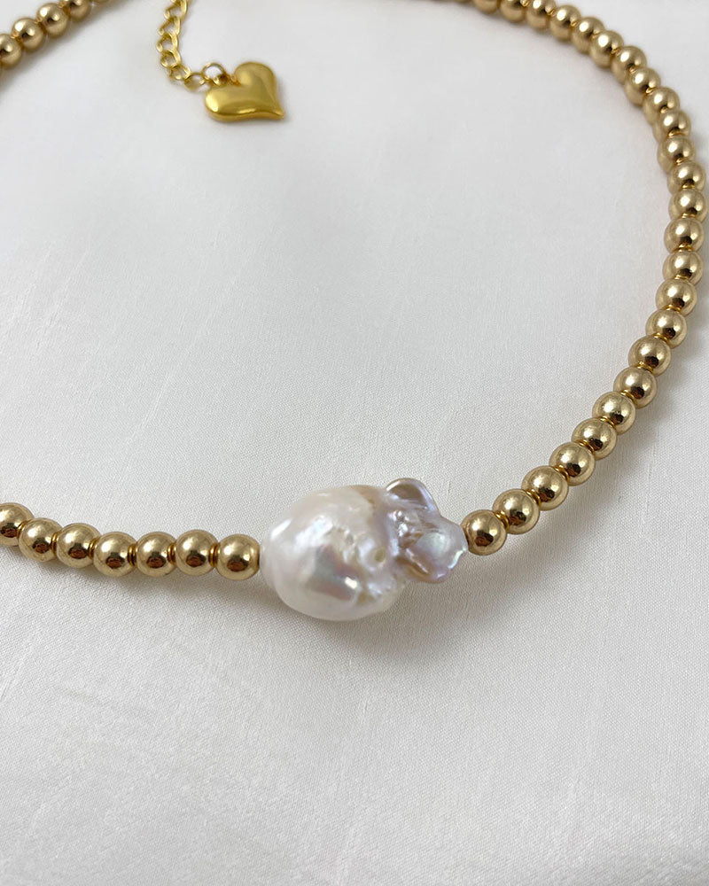 A handmade necklace with gold hematite beads and a large baroque pearl in the middle