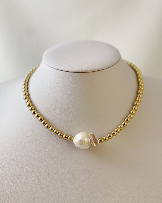 A handmade necklace with gold hematite beads and a large baroque pearl in the middle