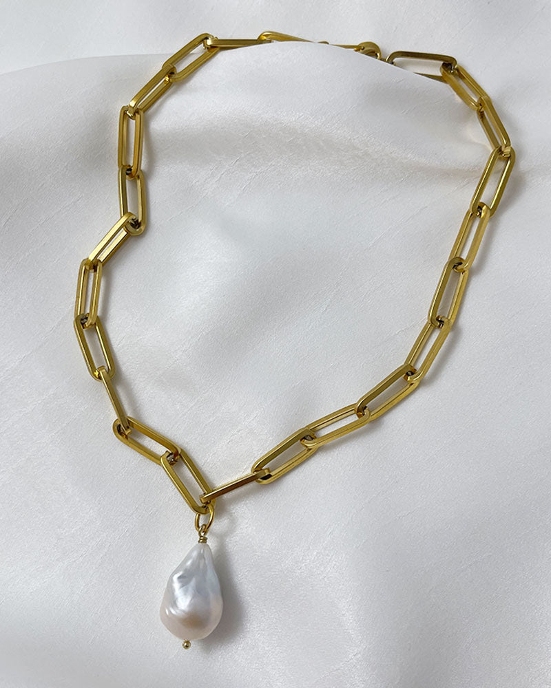 A gold chunky chain necklace with a large baroque pearl in the middle