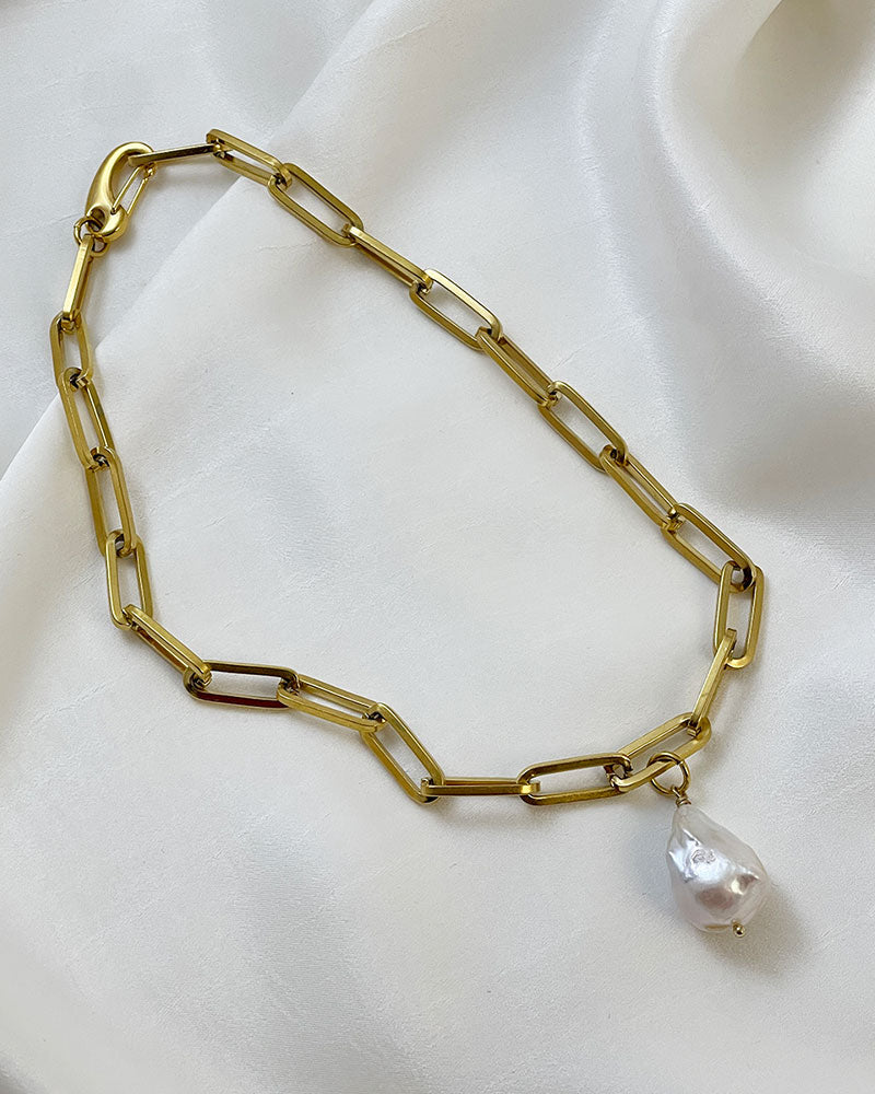 A gold chunky chain necklace with a large baroque pearl in the middle