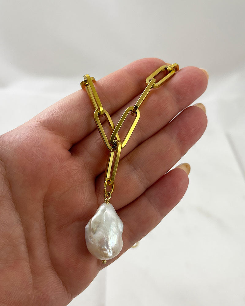 A gold chunky chain necklace with a large baroque pearl in the middle