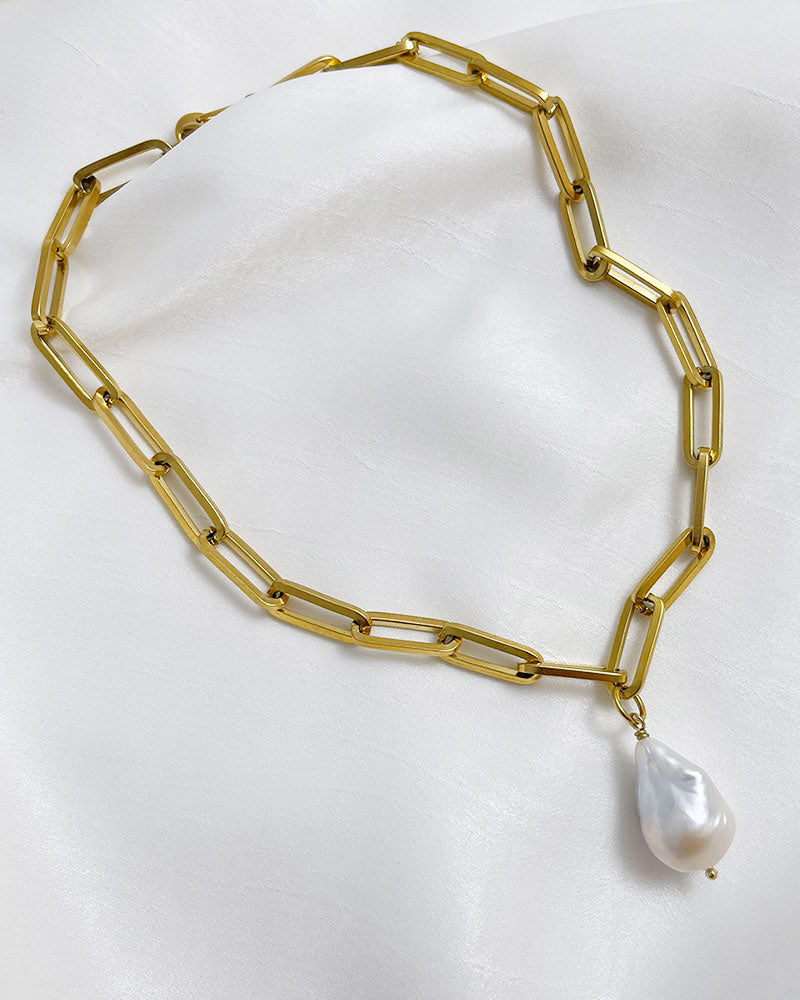 A gold chunky chain necklace with a large baroque pearl in the middle