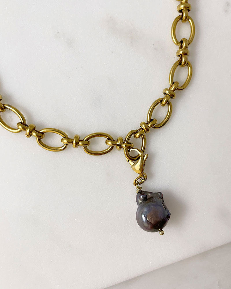 Close-up look of a gold chunky chain necklace with a removable large black baroque pearl in the middle