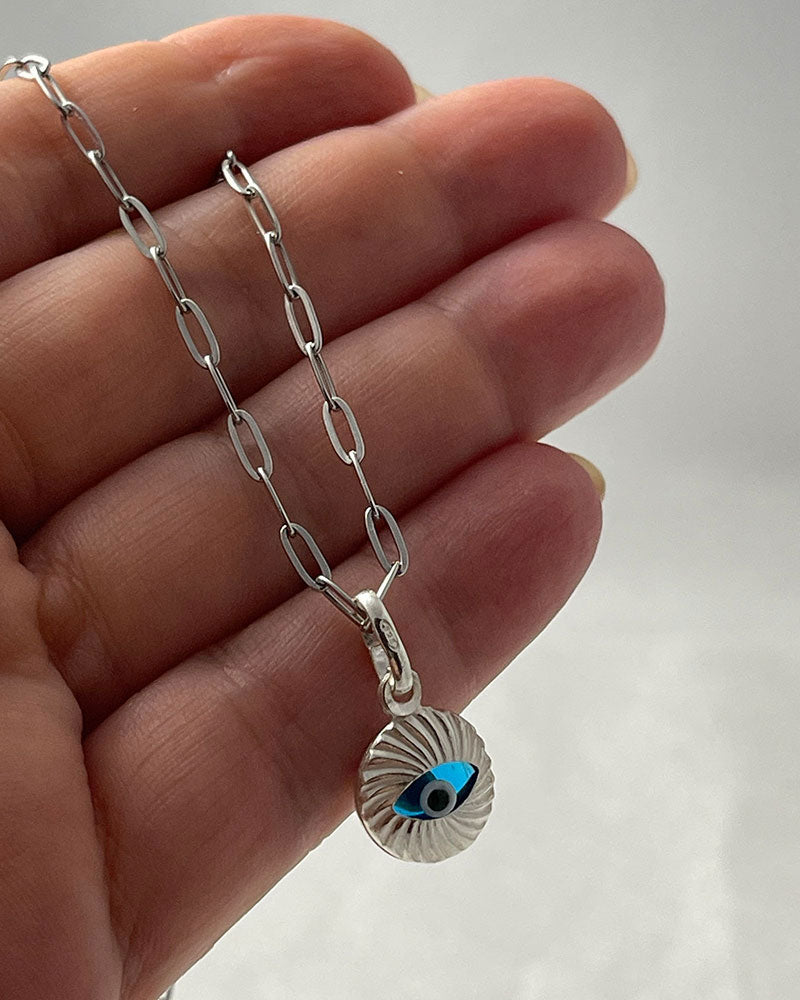 A silver paperclip chain necklace with a blue and silver evil eye pendant. The pendant is round and has a textured surface.