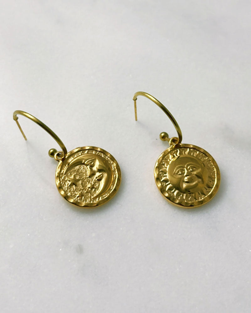 The Sun Moon Hoop Earrings, a pair of gold open hoop earrings featuring a round double faced sun moon charm.
