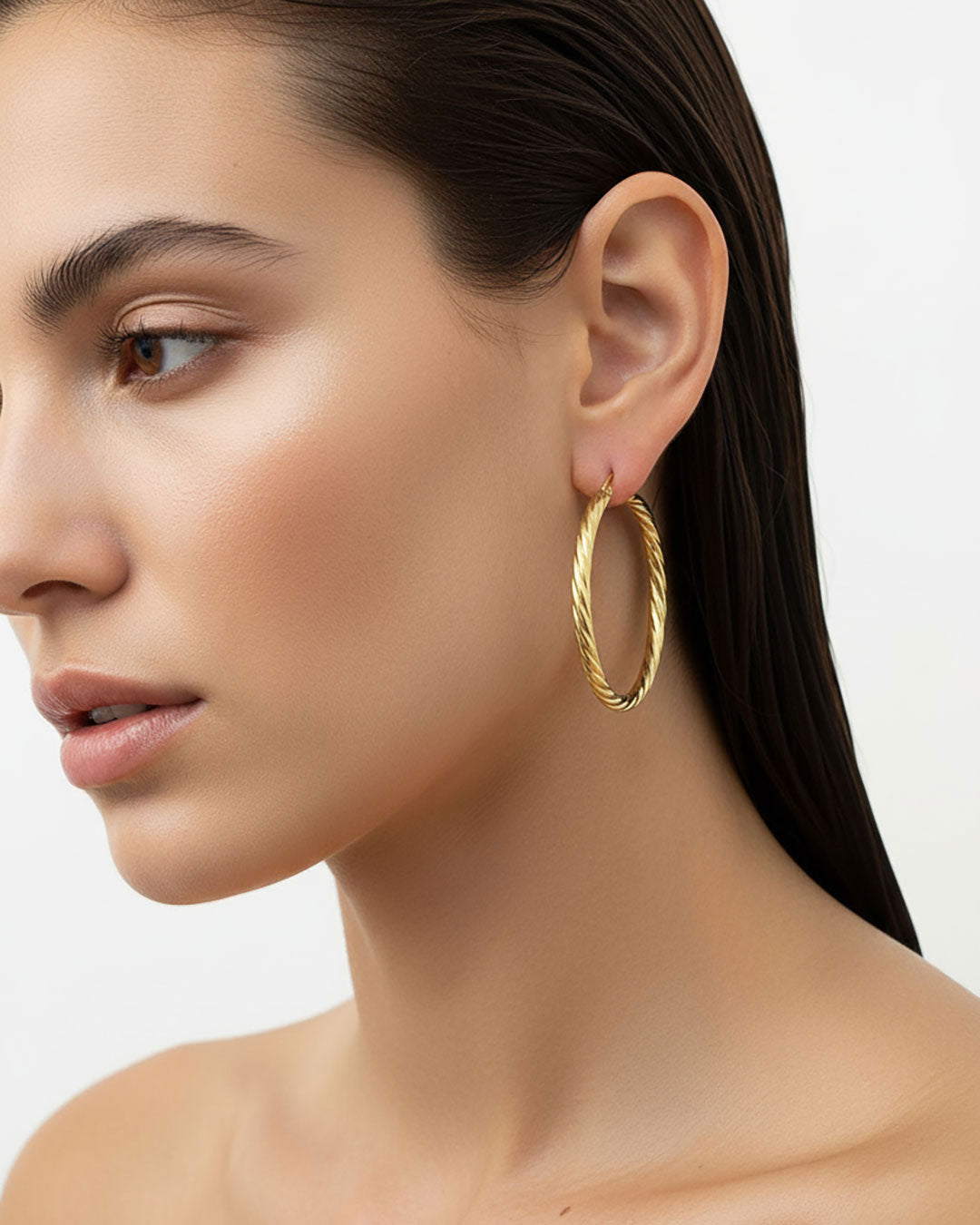 Close-up of a woman wearing gold twisted hoop earrings