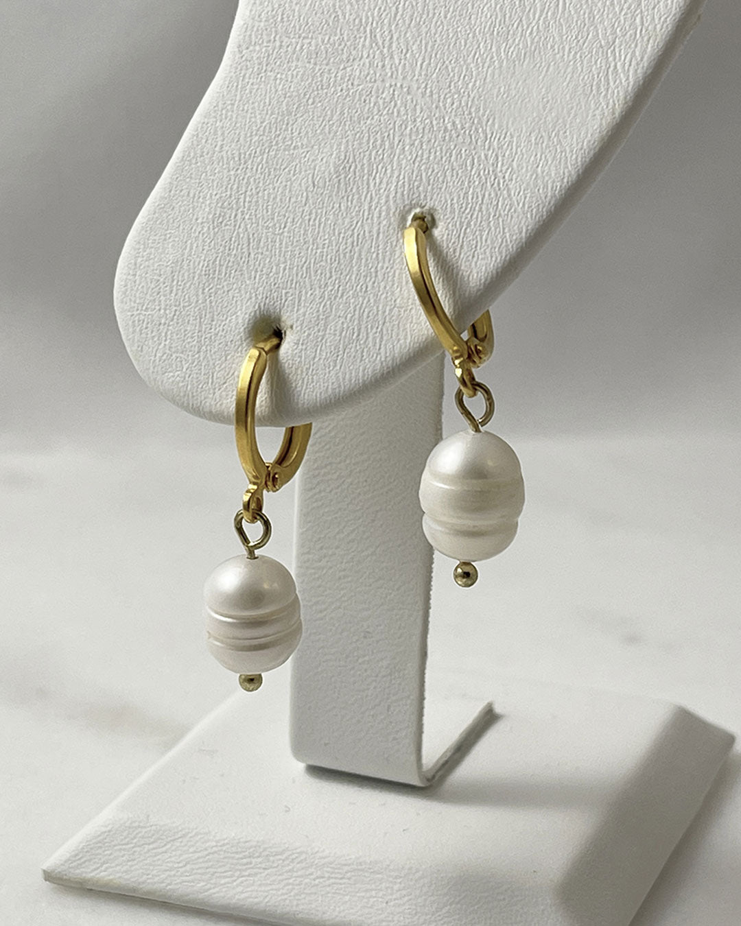 The Audrey Pearl Hoop Earrings, a pair of gold huggie hoops earrings featuring freshwater pearls.